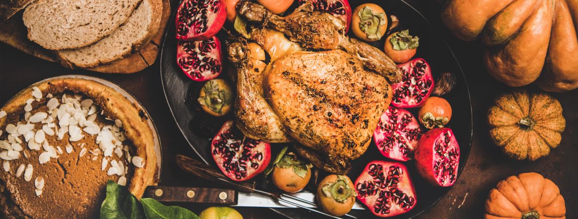 Roasted chicken on table with pomegranates, squash, bread and pie, wide composition