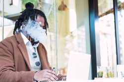 Smoking Black man using laptop on restaurant terrace
