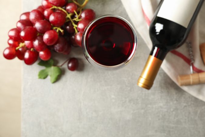 Grape, bottle and glass with wine on grey background, top view