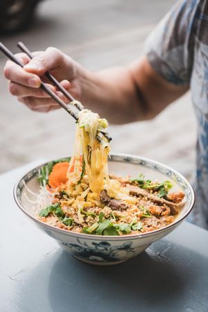 Man eating noodles at Vietnamese restaurant with chopsticks