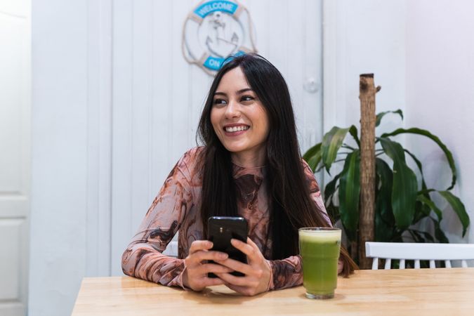 Smiling woman using smartphone at table in bar