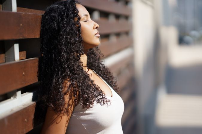A Serene Woman with Beautiful Curly Hair is Joyfully Enjoying the Warm Sunlight Outside