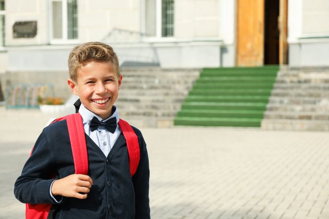 Boy with backpack against school building, space for text