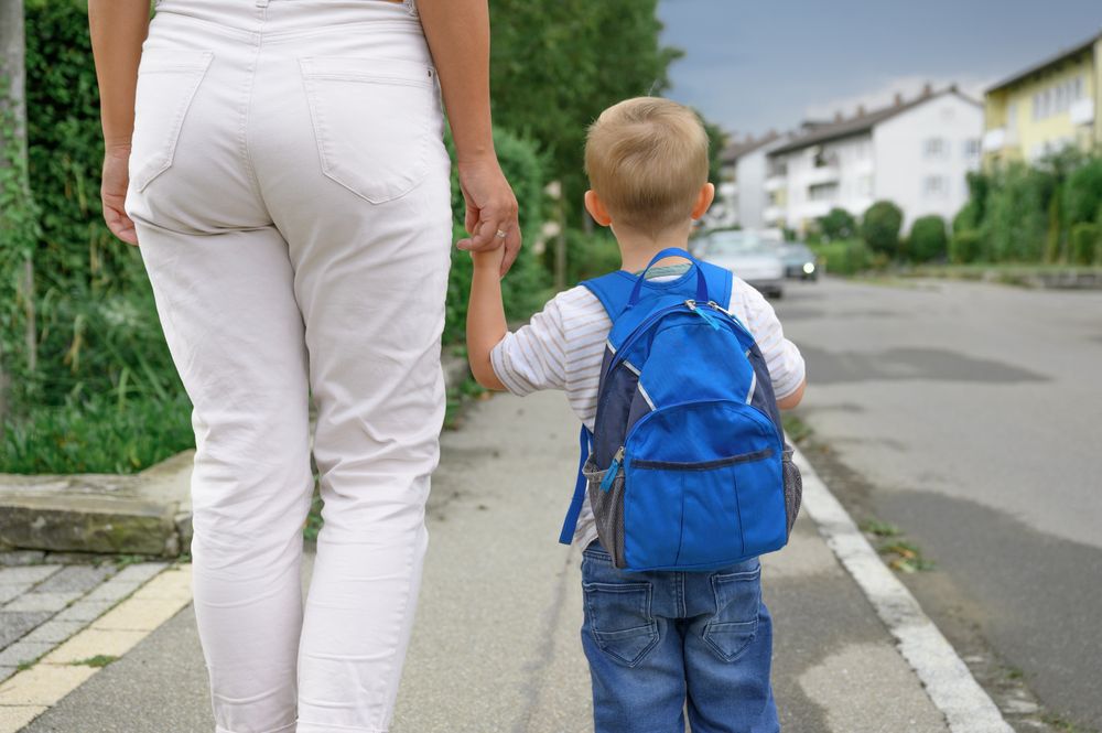 Unrecognizable boy with backpack walking on street with mother