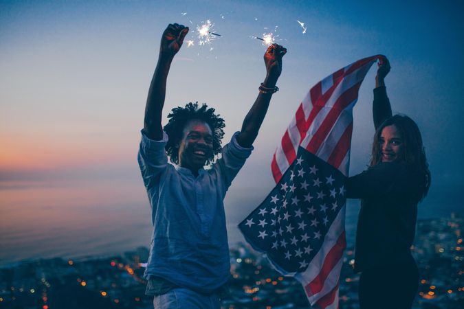 Smiling couple with sparklers and the American flag at dusk