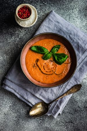 Top view of tomato soup with oil garnish and basil leaves served with peppercorn