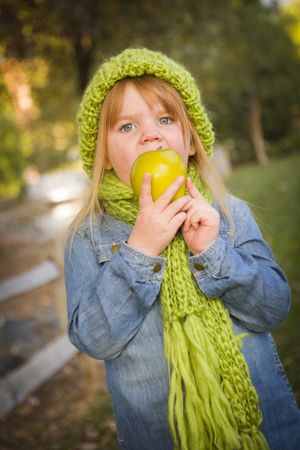 Young Girl Wearing Green Scarf and Hat Eating Apple Outside