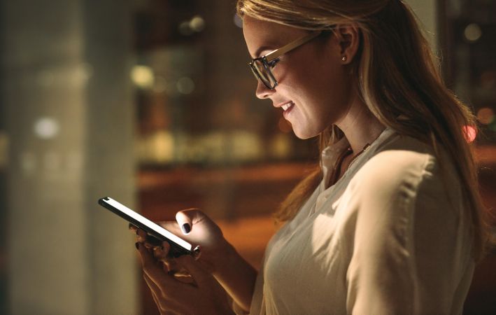 Side view of happy woman looking at her smart phone and smiling at night