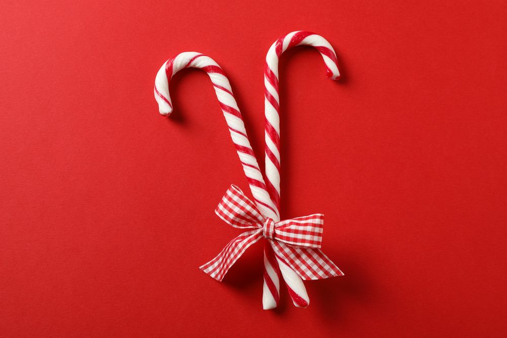 Sweet candy canes with bow on red background, space for text
