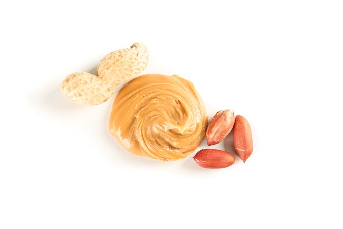 Creamy peanut butter and peanut isolated on light background, top view. A traditional product of American cuisine