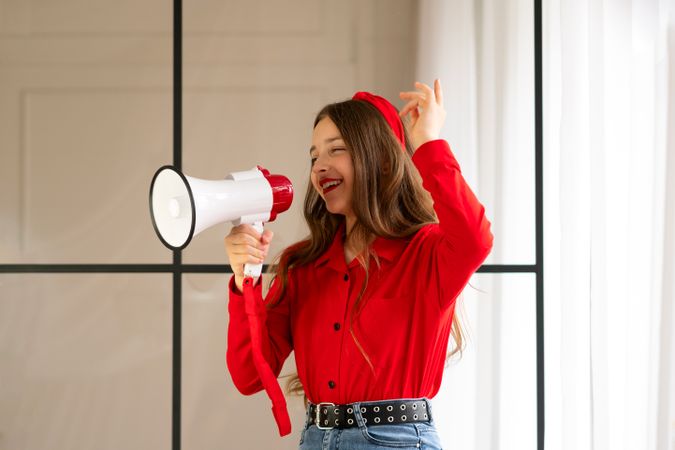 Cheerful teen girl speaking into megaphone in bright interior.