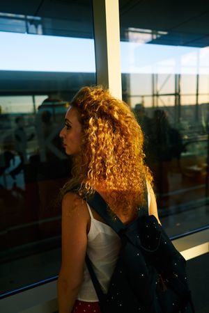 Young woman thoughtfully looking at airplanes through window in sunlight