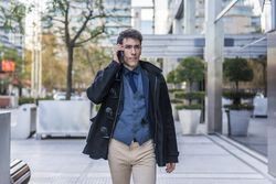 A handsome businessman talking on his cell phone while walking in the street