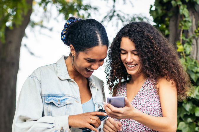 Black Latina friends using a smartphone in the park.