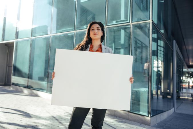 Confident businesswoman holding blank banner standing outside in front of urban office