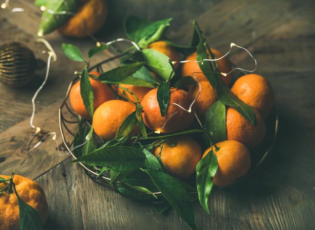 Freshly picked tangerines with leaves in wire bowl on wooden table