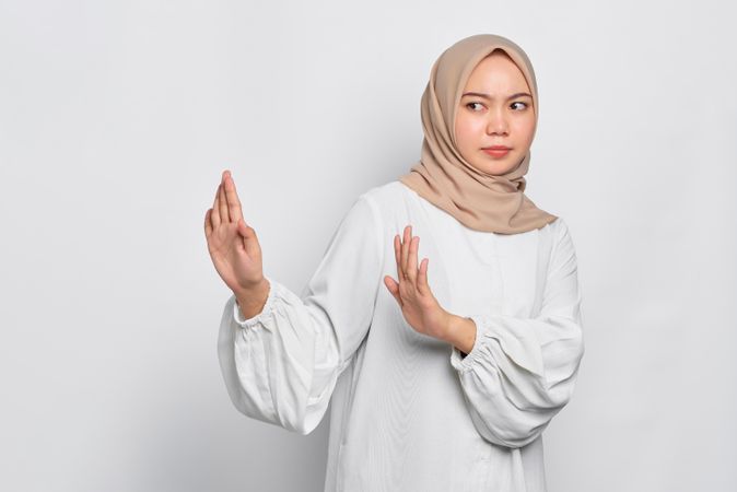 Stern Asian female in headscarf with hands up saying no