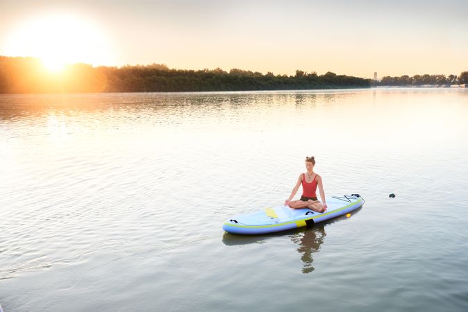 Woman sitting cross legs on paddle board in the middle of a lake