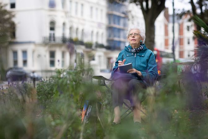 Older grey haired woman sitting outside drawing in field