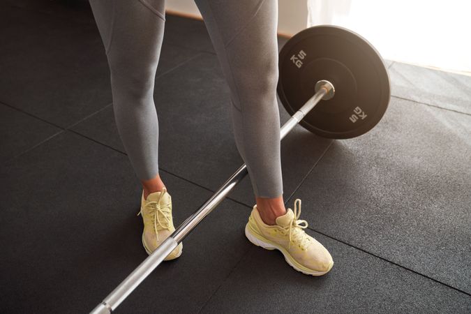 Crop sportswoman exercising with barbell in gym