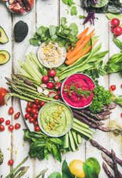 Fresh colorful vegetables and dips with hummus, avocados, asparagus, carrots on wooden table