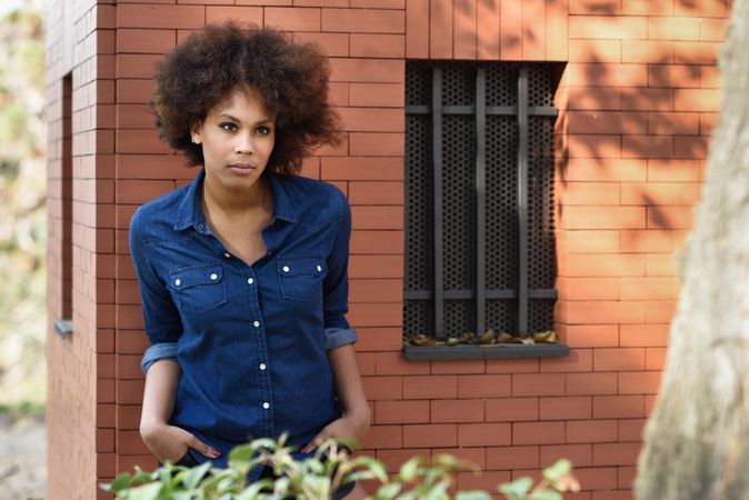 Female leaning on building with hands in her pocket, copy space