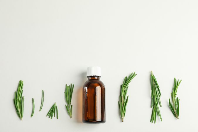 Flat lay composition with rosemary oil and leaves on plain background, space for text