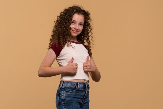 Young girl showing thumbs-up pose, smiling confidently
