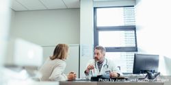 Male physician talking to a patient during consultation at his office 5QxZ90