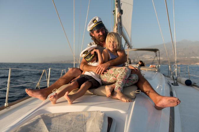 Man hugging smiling children and sitting on deck of yacht in sea
