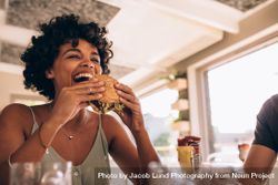 Black woman about to bite into a burger at a restaurant 0JOdw5