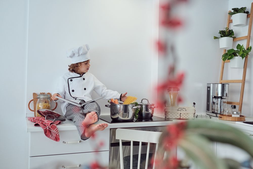 Adorable preteen boy in chef suit reading culinary book