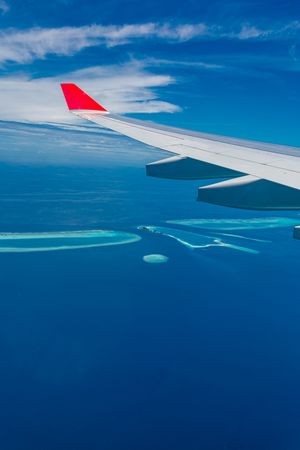 Airplane wing against a blue sky above, and blue sea below