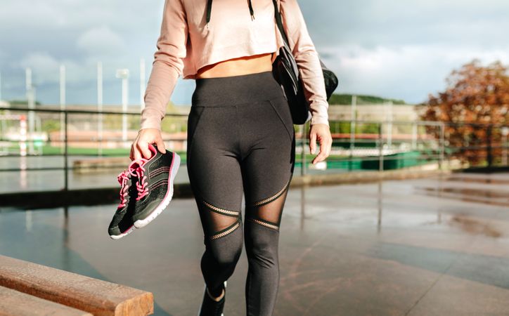 Unrecognizable sportswoman with gym bag and sports shoes walking to go to training