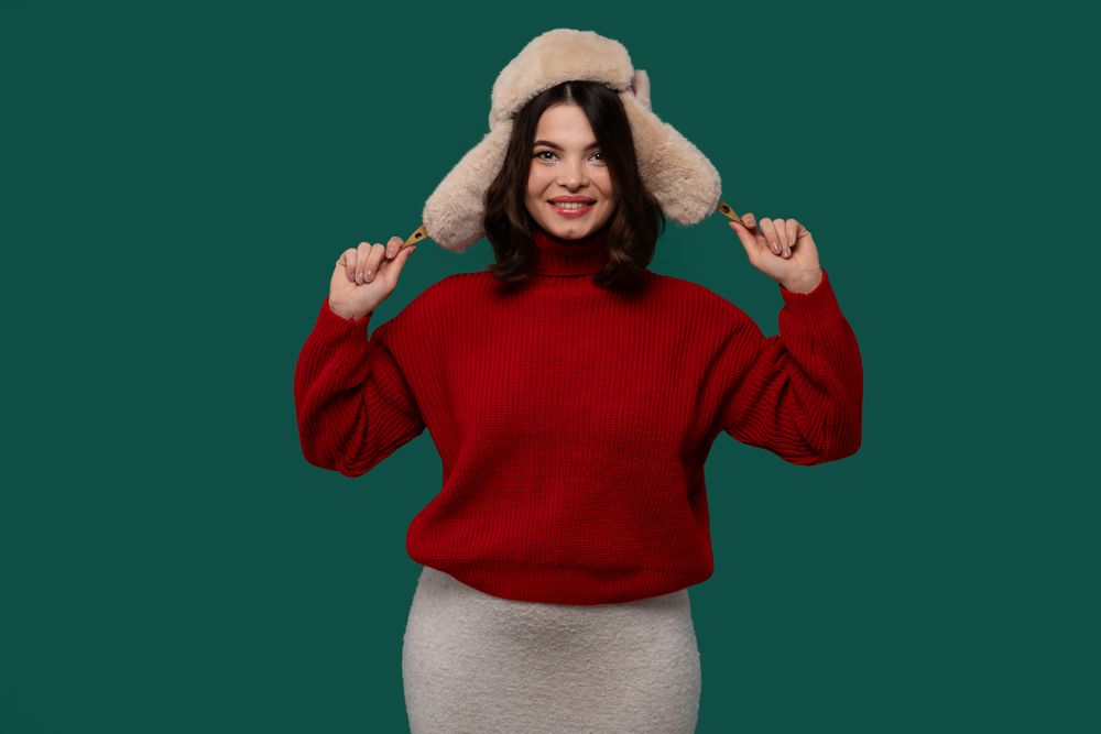 Smiling woman in red sweater adjusting fluffy fur hat