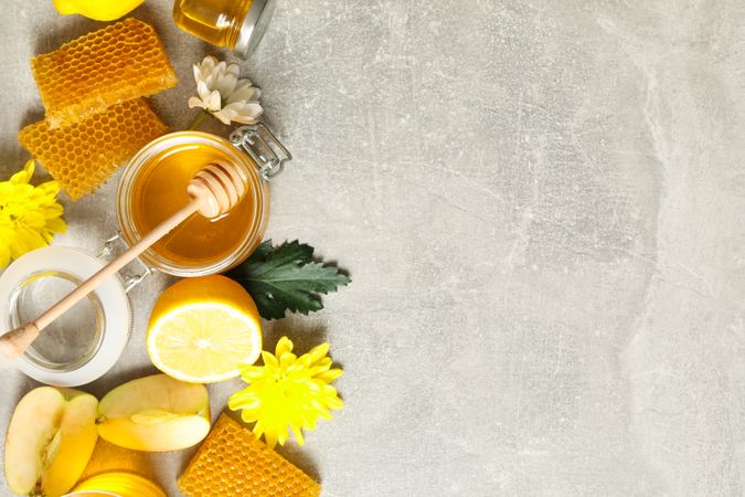 Flat lay with honey, flowers and fruits on grey background, copy space