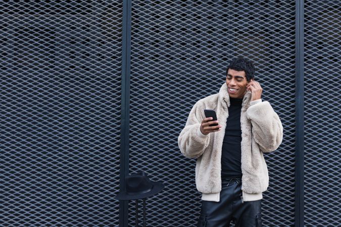 Content stylish hispanic man with smartphone in earbud on street