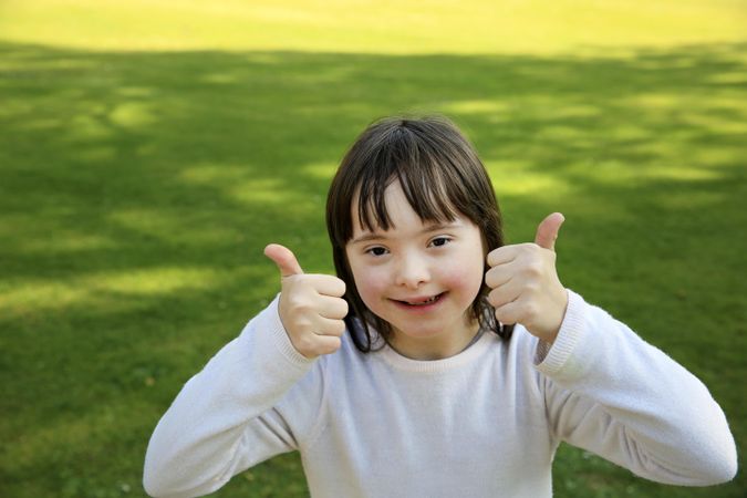 Little girl at grassy park giving thumbs up