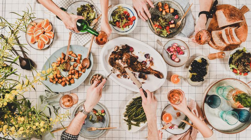 Flat-lay of hands of people eating roasted lamb, and pouring wine