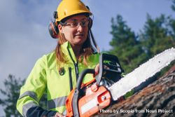 Woman in yellow helmet and vest wearing eyeglasses and using a chainsaw 498Pv5
