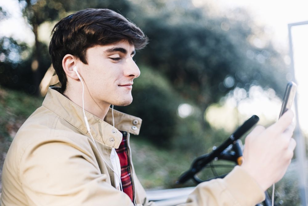 Man sitting on bench outside next to bike watching something on phone