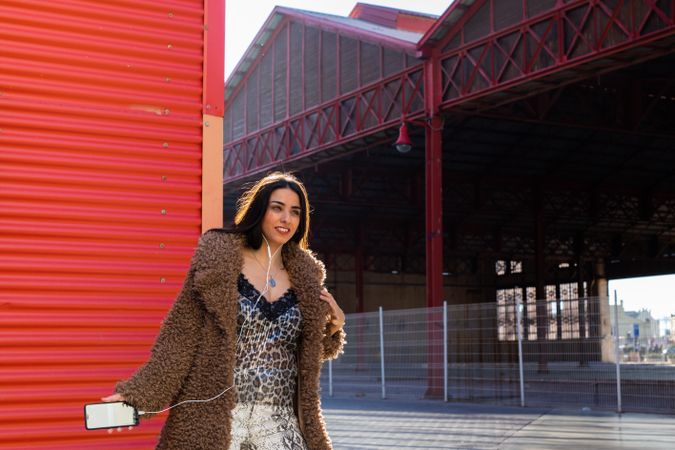 Trendy woman with smartphone near wall