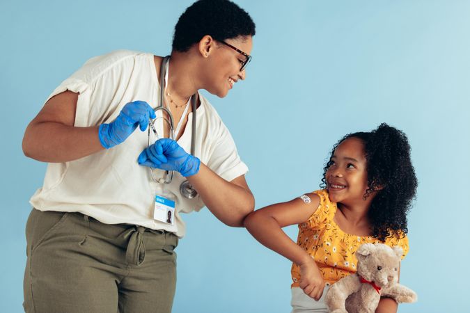 Doctor giving elbow bump to girl after vaccination in clinic