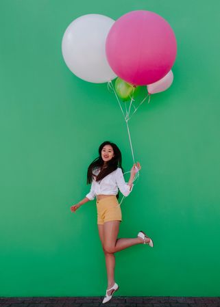 Joyful young woman jumping up holding a bunch of balloons