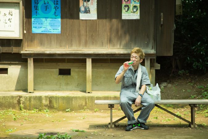 Man in work suit drinking juice and sitting on wooden bench outdoor
