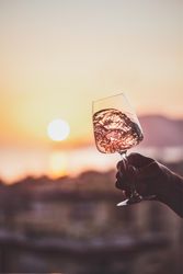 Man's hand swirling glass of rose wine against sunset, vertical composition