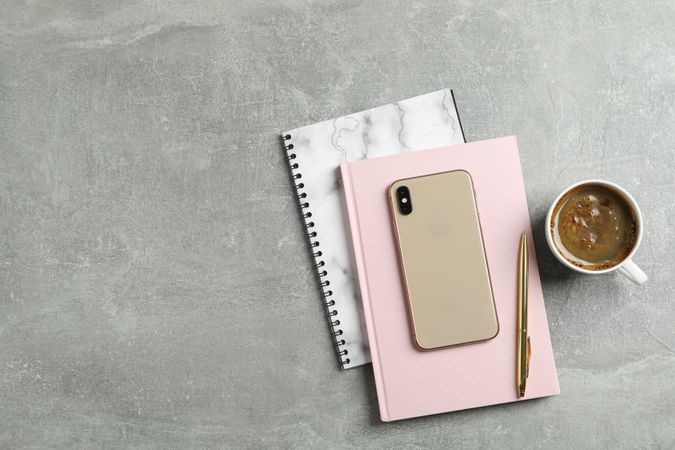 Cup of coffee with copybooks, phone and pen on grey background, top view