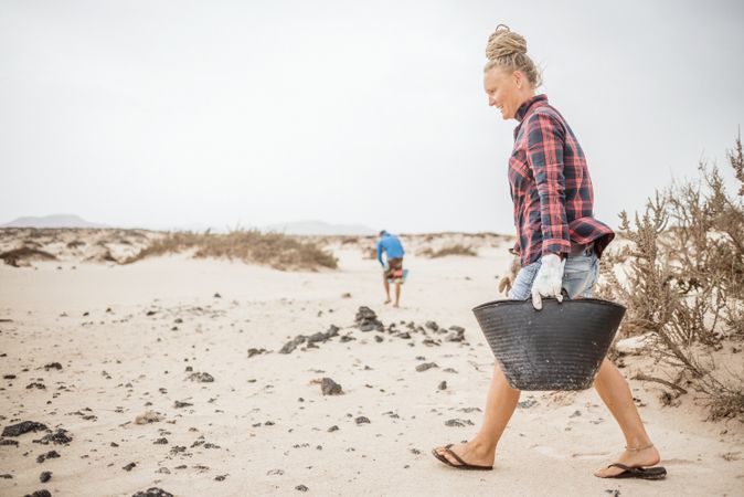 Content modern woman picking litter from sandy seashore