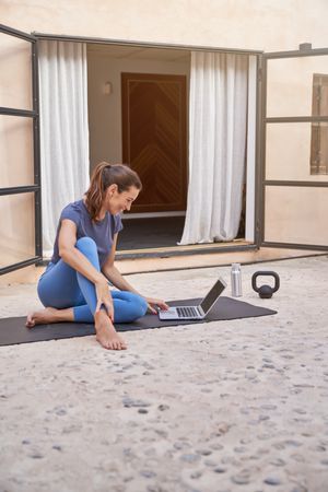 Smiling sportswoman using laptop on yoga mat