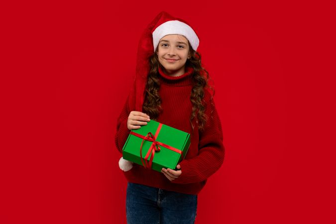Smiling girl in Santa hat holds green Christmas gift